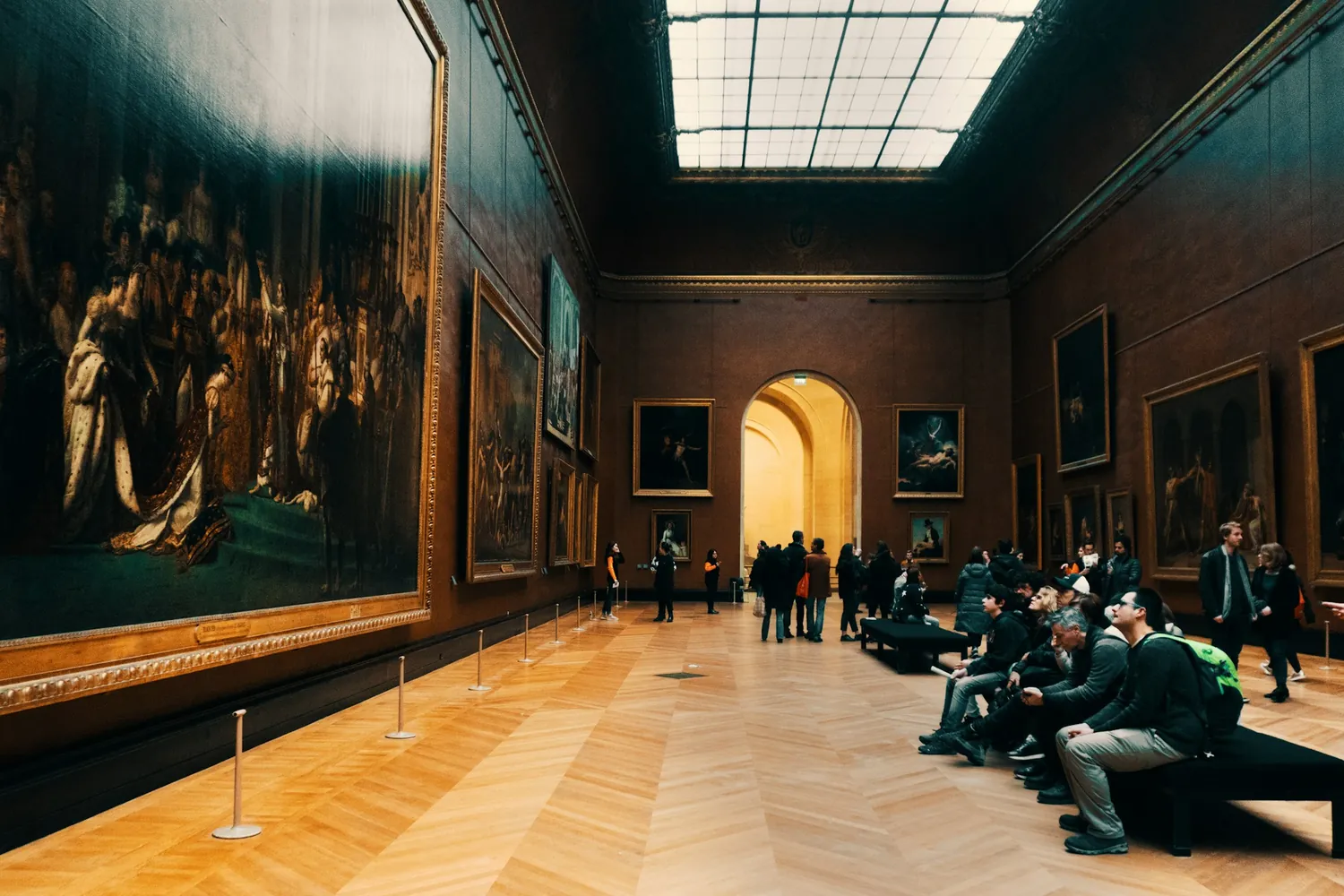 Visitors in a grand museum gallery lined with classical paintings.