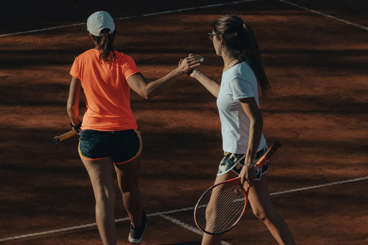 Two tennis partners sharing a high five on a clay court at their club.