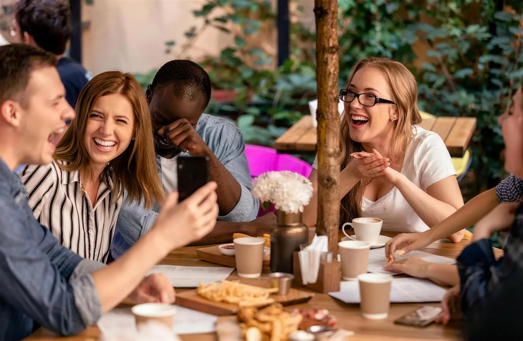 Friends laughing together over coffee at a café terrace, sharing ideas.