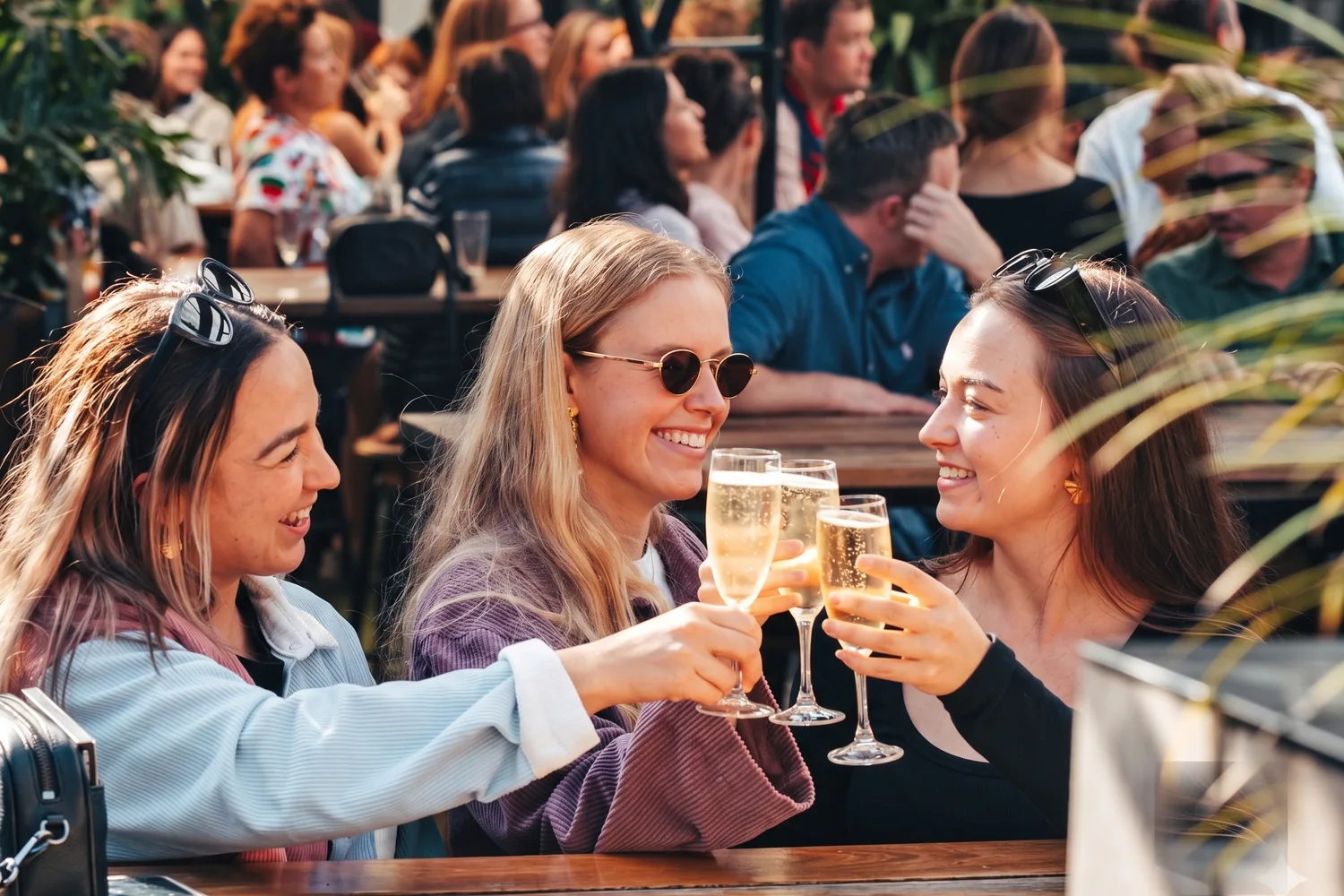 Friends raising a toast together on a sunny café terrace.