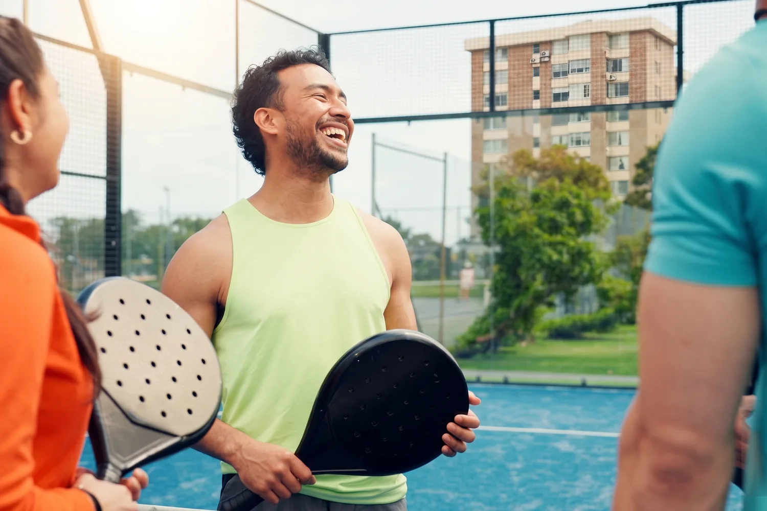 Friends laughing together with paddles at a padel court.